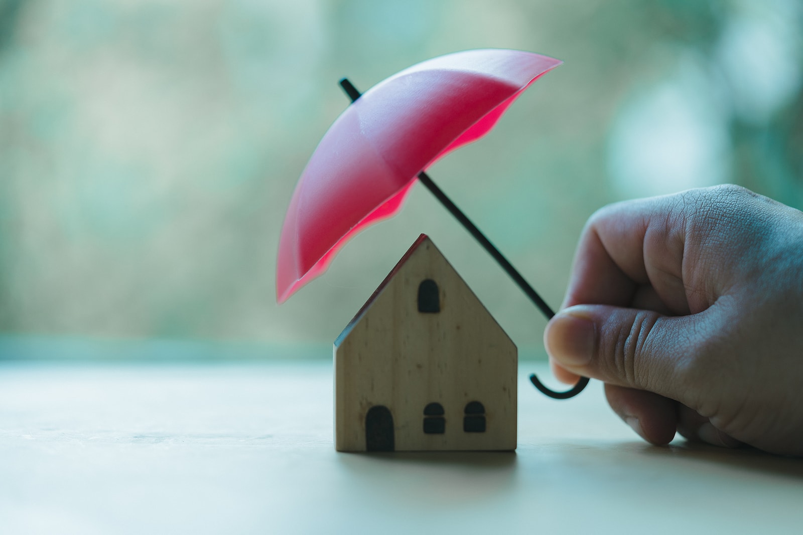 Hand Holding Red Toy Umbrella Covered House. House Insurance Concept.